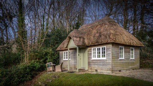 Durgan Wood Cottage, a small timber cottage with thatched roof with a sloped garden, Cornwall